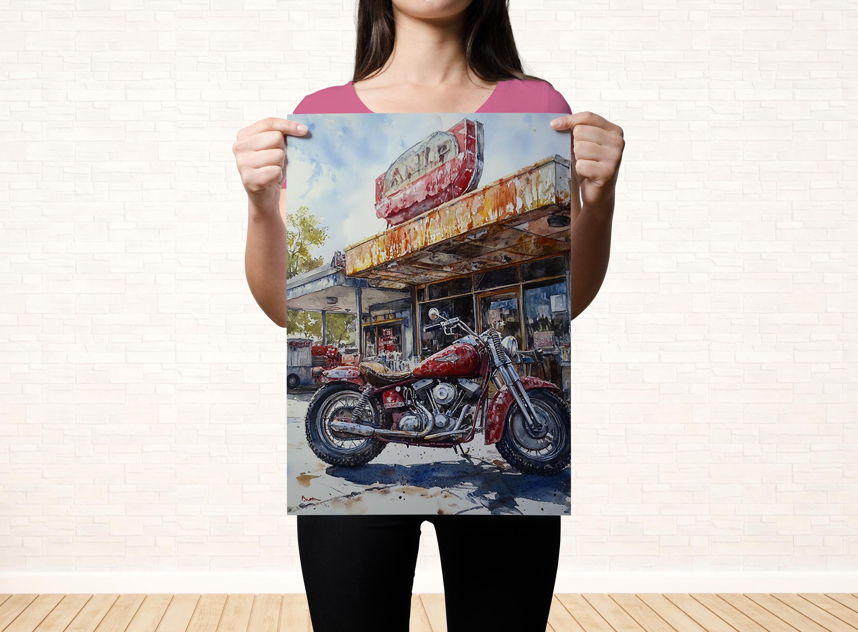 A woman holds up a framed print of a red motorcycle parked in front of a dilapidated diner with a faded sign.